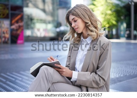 Woman working, writing down thoughts in her planner, sitting in city centre in business clothing. Royalty-Free Stock Photo #2230814357