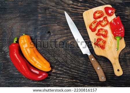 Fresh raw sweet pepper (bell pepper) on a cutting board with a knife. Chopped pepper pieces are ready to cook. Dark wooden table, top view.Space for text.