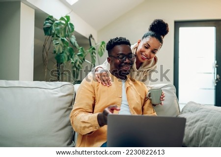 Portrait of a diverse couple enjoying time at home and using laptop. African american man and hispanic woman hugging and looking into the screen. Modern interior. Copy space. Royalty-Free Stock Photo #2230822613