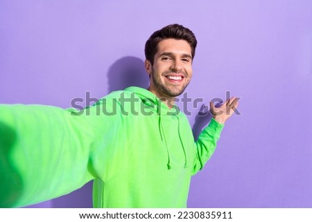 Portrait of pleasant confident guy with brunet hairstyle dressed green hoodie doing selfie copy space isolated on violet color background