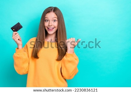 Photo of girl teenager wear yellow sweater hold bank card finger direct new offer empty space shopping mall isolated on aquamarine color background