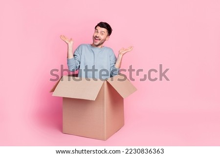 Full size photo of handsome young man sitting inside carton package raise hands wear stylish blue outfit isolated on pink color background