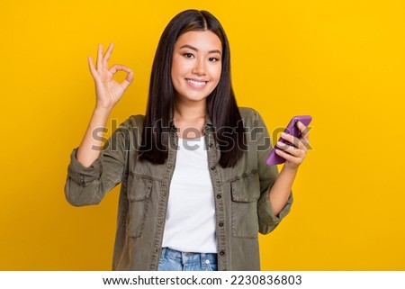 Photo of nice pretty gorgeous satisfied woman brunette hair wear gray shirt hold phone showing okey isolated on yellow color background
