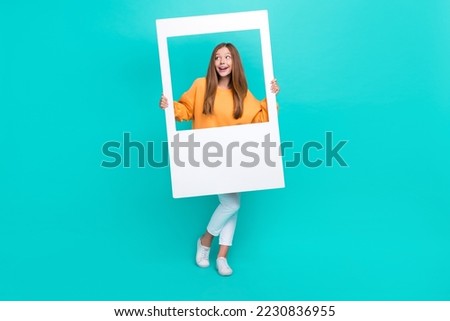 Full length photo of adorable dreamy school girl dressed orange hoodie tacking photo looking empty space isolated teal color background