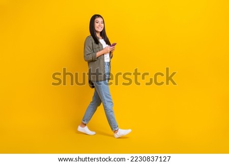 Full length size photo of young successful cute korean lady wear khaki casual outfit hold smartphone distance job isolated on yellow color background