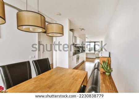 Contemporary minimalist style interior design of light studio apartment with wooden table and chairs in dining zone between open kitchen and living room with white walls and parquet floor Royalty-Free Stock Photo #2230838779