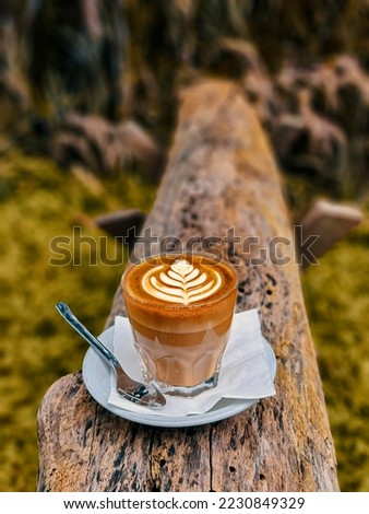 Selective focus of a cup of latte coffee with a picture of roseta on foamy coffee cream on wood log as background 
