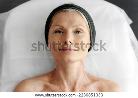 Top view of smiling senior woman laying at the couch after making an effective facial procedure. Lady looking at the camera. Stock photo 