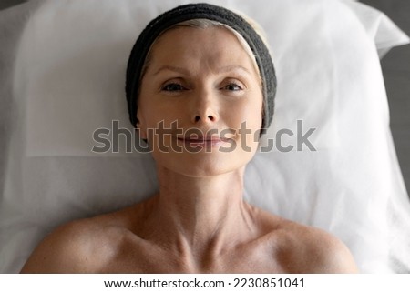 Mature woman laying at the couch and smiling while making beauty procedures top view. Senior lady enjoying of beauty routine. Stock photo 