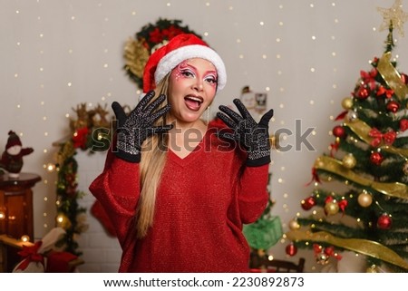 Portrait of young woman with Christmas make-up, wearing Santa Claus hat with astonished expression.