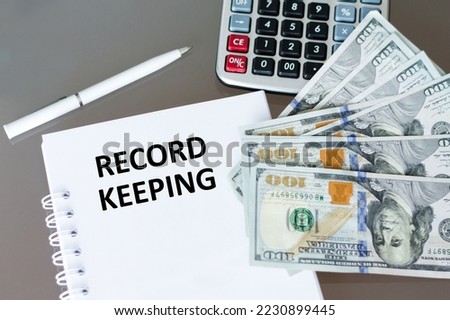 RECORD KEEPING text on a notepad on a table next to a pen, dollar bills and a calculator