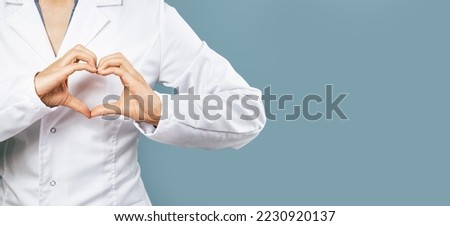 Female doctor in white uniform forms a heart shape with her hands. Minimal on blue background. Banner copy space. Heart, cardiology and medical care support and assistance female health gynecology