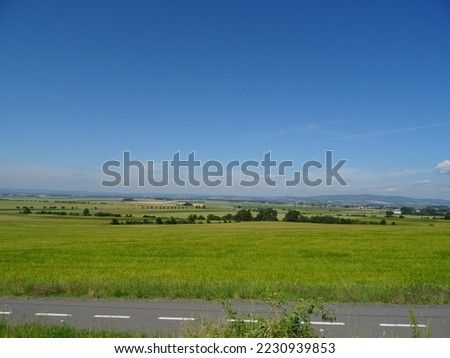  a road going through a green field with a sky background and a road sign in the foreground that says. . 