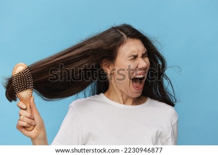 a sad woman combs her hair with a wooden massage comb with a sad face. Horizontal photo on a light blue background