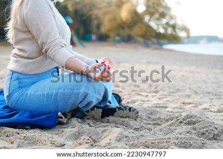 A young woman on the beach in jeans and a sweater sits in a lotus position. Hands close up. Horizontal photo