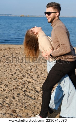 A young bearded man in sunglasses hugs a girl by the waist. Couple having fun and fooling around on the beach. Vertical photo