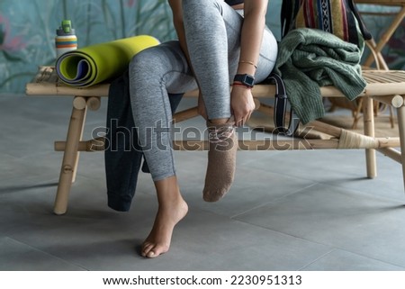 Close-up multiethnic woman putting on clothes after fitness training over green domestic house plant loft blue home background. Lifestyle concept. Copy space, mock-up. Eco natural, body conscious