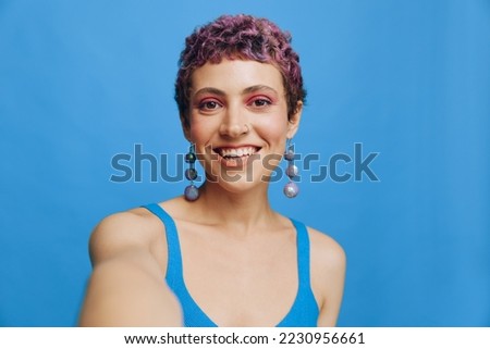 Young sports woman fashion blogger takes a picture of herself on the phone in blue sportswear smiling and looking at the camera on a blue monochrome background