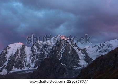 Awesome landscape with sunset pink reflection on huge snowy mountain top in violet dramatic sky. Hanging glacier and cornice on giant snow mountains in dusk. Snow-covered mountain range in twilight. Royalty-Free Stock Photo #2230969377