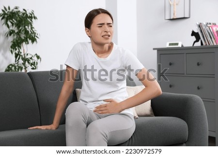 Young woman suffering from cystitis on sofa at home Royalty-Free Stock Photo #2230972579