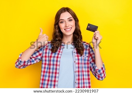 Photo of pretty confident lady wear plaid shirt holding plastic card showing thumb up isolated yellow color background