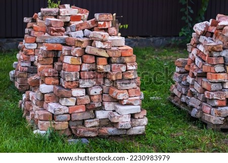 A stack of red clay bricks on a grass. Royalty-Free Stock Photo #2230983979