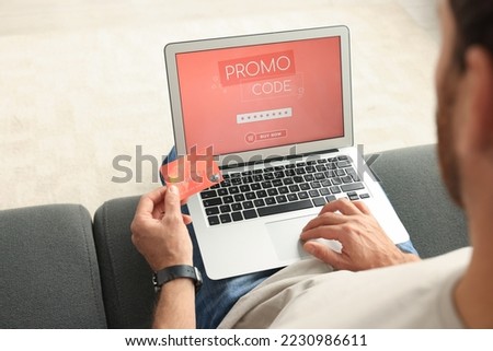 Man holding laptop with activated promo code and credit card on sofa, closeup
