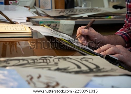 A calligrapher writing with pen and ink. man hands writing arabic calligraphy with ink. Arabic and Persian calligraphy. Writing Nastaliq calligraphy. Calligraphy training. Close-up of Arabic reed pen Royalty-Free Stock Photo #2230991015