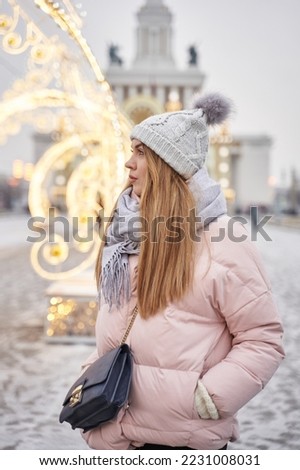 a young woman looks away in winter against the backdrop of the lights of a decorated city for Christmas
