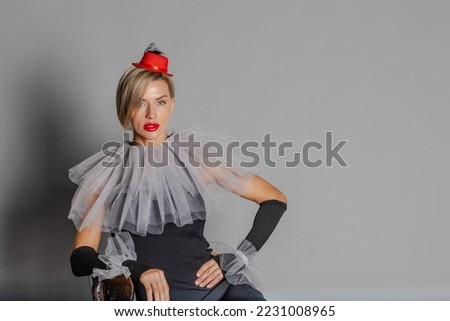 Elite clown. Woman dressed as clown black dress with harlequin collar and red hat. Contrast image on grey background. High quality photo