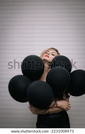 Beautiful woman of model appearance with dark balloons. Art shooting from unusual angles. High quality photo