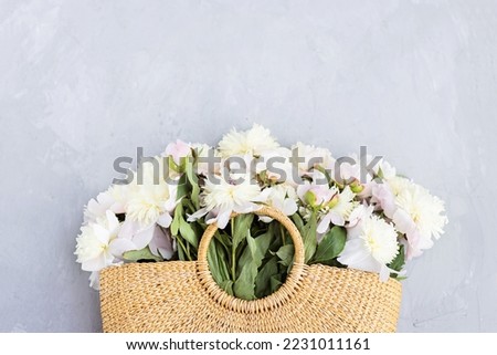 Beautiful white peony flowers in wicker bag on gray concrete background, copy space for your text, top view, flat lay style. Happy mothers day greeting card mockup. International Woman Day. Valentines