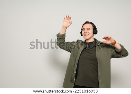 Handsome young man with headphones dancing on light grey background. Space for text