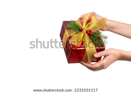 Female hand with shiny red Christmas gift box decorated with a golden bow and fir twigs, close up, isolated on white. Holiday, New Year, present, love, care, congratulation, surprise concept.