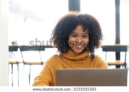 Photo of cheerful joyful mixed race woman in yellow shirt smiling work on laptop talk speak video call online. Smart ethnic female in earphones study distant on computer at home. Education concept.