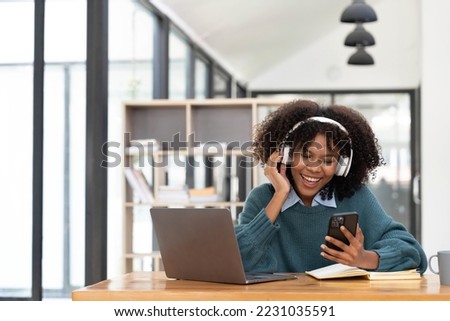 Photo of cheerful joyful mixed race woman playing games and wearing wireless headphones at home Play game on your smartphone that wins the moment of victory. Fun and enjoyable vacation