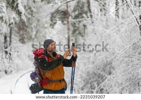 Middle aged hiker in winter forest taking a photo with his mobile phone.