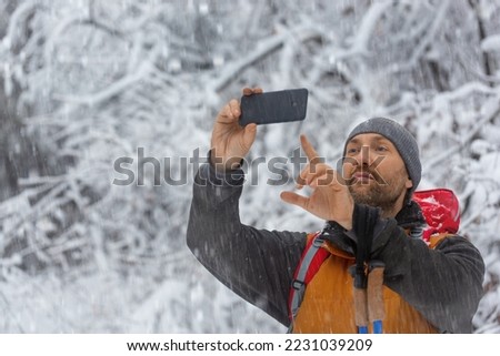 Middle aged hiker in winter forest taking a photo with his mobile phone. Close-up photo.
