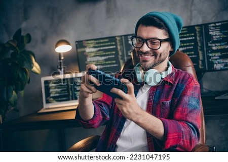 Photo of funny positive freelancer wear hat glasses headphones watching video modern device indoors workplace workstation loft