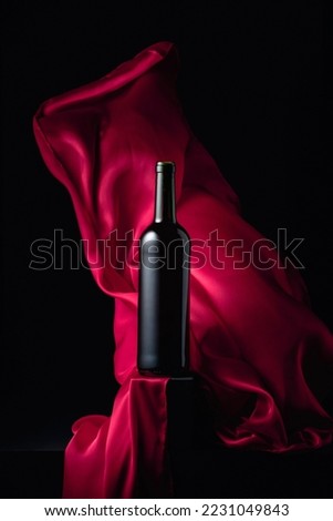 Вottle of red wine on a black background with flutters red cloth.