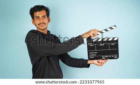 Cheerful Young Asian Indian man standing holding clapperboard, clapper board used in film making, isolated on colour background studio portrait