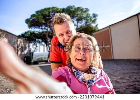 Disabled woman on wheelchair taking selfie with man at park - Happy family having fun together outdoors - Son and mother trying to take a crazy picture - Focus on woman