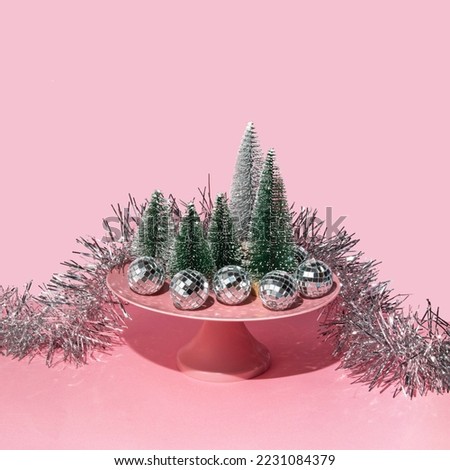 Christmas trees, ornaments and cake plate stand on pastel light pink background. Minimalistic New Year concept. Creative Xmas composition.