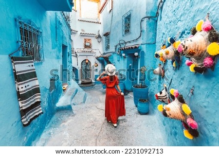 Young woman with red dress visiting the blue city Chefchaouen, Marocco - Happy tourist walking in Moroccan city street - Travel and vacation lifestyle concept Royalty-Free Stock Photo #2231092713