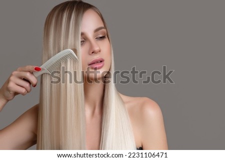 beautiful young woman holds a comb in her hands. Blonde woman with long straight hair on a gray background Royalty-Free Stock Photo #2231106471