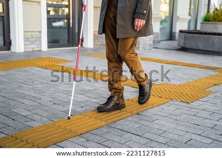 Blind man with a walking stick. Walks on tactile tiles for self-orientation while moving through the streets of the city Royalty-Free Stock Photo #2231127815