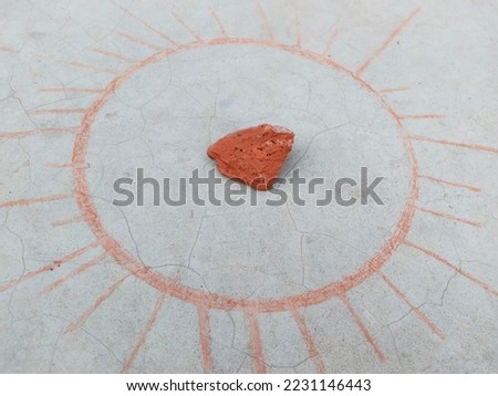 sketching a circle on surface with shattered brick or chalk. Round shape picture has been made on the ground with a piece of brick. Drawing of red circle is being made by drawing a line on the ground.