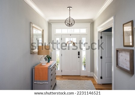 An open large and wide interior front door hallway foyer with transom, hanging light fixture, coastal colors and entry way table and wood floors. Royalty-Free Stock Photo #2231146521