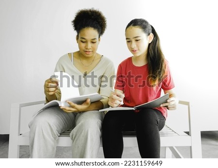 Diversity teenage students sitting at a bench reading, and learning lesson from textbook preparing for educational exam. Teenage girls concentrate doing homework together after studying at school.