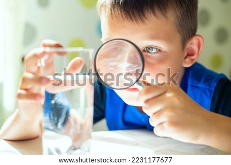 The child boy looking at water in a glass through magnifying glass Royalty-Free Stock Photo #2231177677